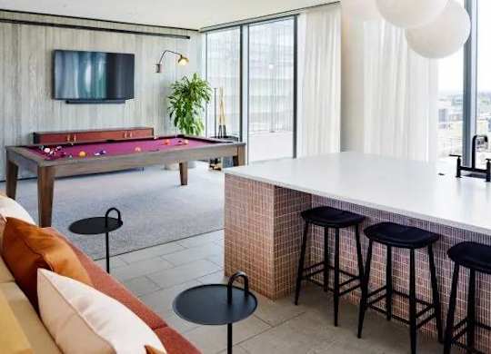 A room with a pool table, bar stools, and a television.