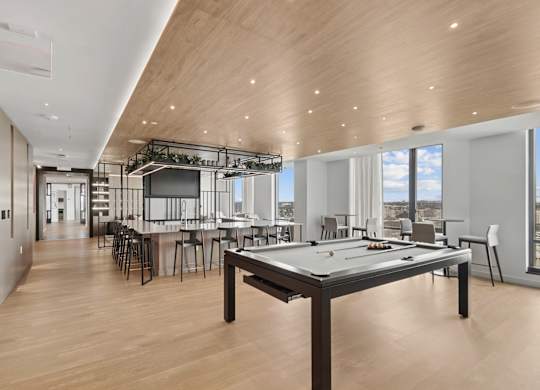 A billiard table is in the middle of a room with a bar and a kitchen in the background.