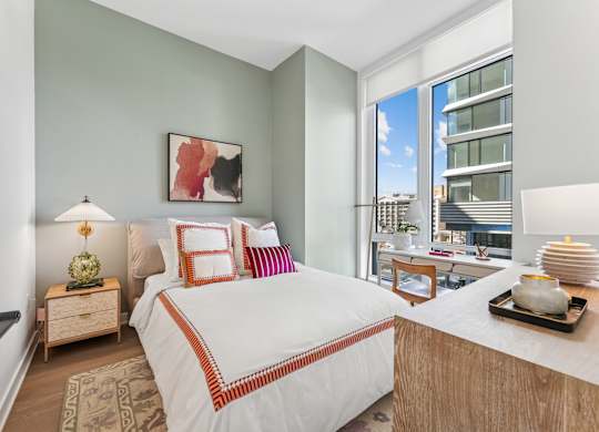 A bedroom with a large bed and a view of a cityscape through the window.