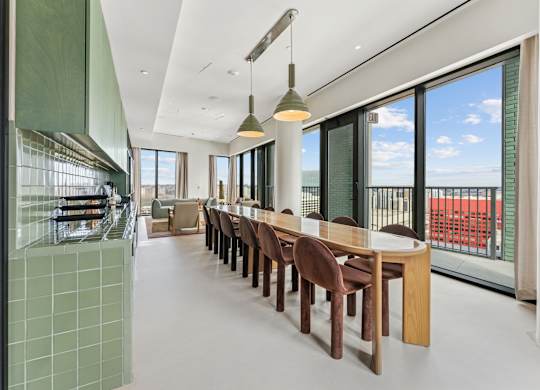 A long table with chairs is in a room with a glass wall.