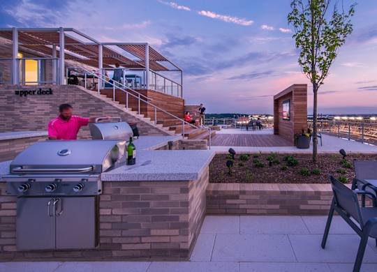 A woman in a pink shirt is standing on a patio with a grill.