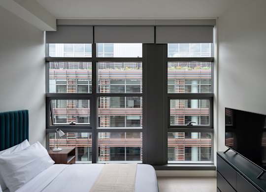 A bedroom with a large bed, a television, and a window overlooking a building.