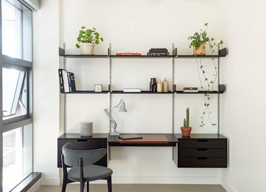 A grey chair sits in front of a desk with a computer and a plant on it.