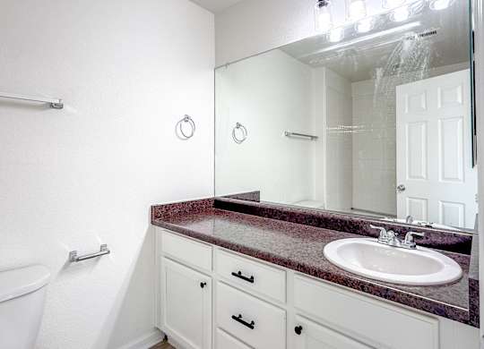 A bathroom with a marble countertop and white cabinets.