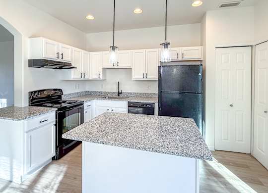 A kitchen with a granite countertop and a black refrigerator.