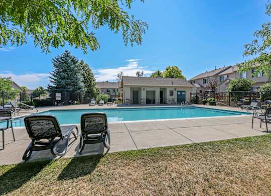Two lounge chairs sit on the lawn in front of a pool and a house.