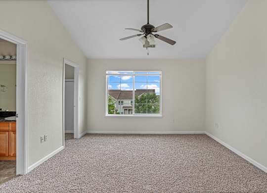 A room with a ceiling fan and a window showing a house outside.