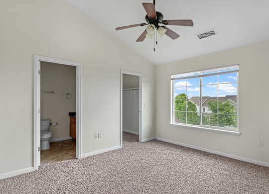 A room with a ceiling fan and a window overlooking a house.