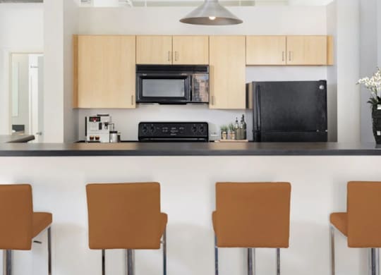 A kitchen with a black fridge and microwave, a black countertop, and brown chairs.