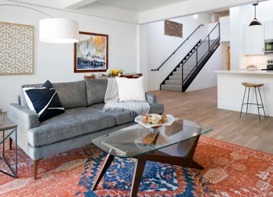 A grey couch with a white pillow and a glass table in front of it.