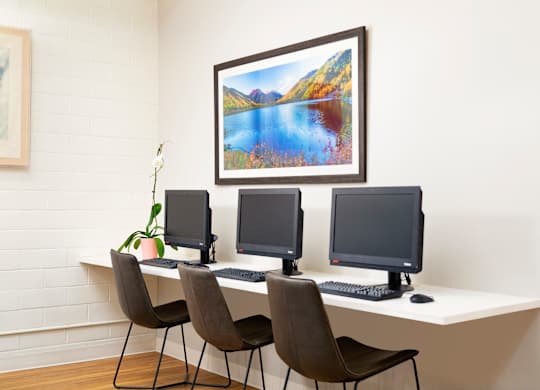 Three computer monitors are on a desk with chairs.