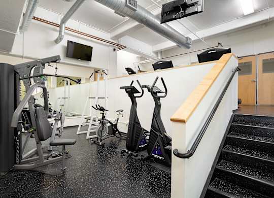 A gym with a variety of equipment including a treadmill, stationary bike, and weight bench.