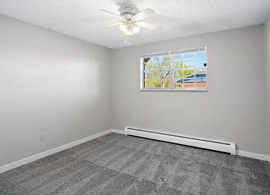 A room with a ceiling fan and a window with a view of a building outside.