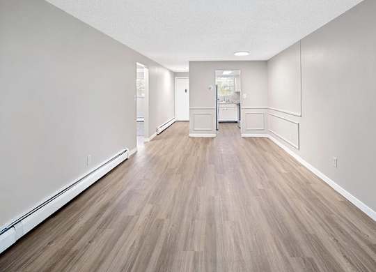 A long, empty hallway with wood flooring and white walls.