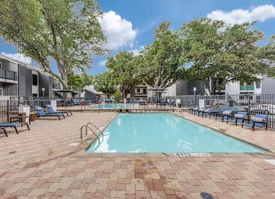 A large outdoor pool surrounded by trees and chairs.