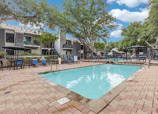 A swimming pool surrounded by a brick patio and trees.