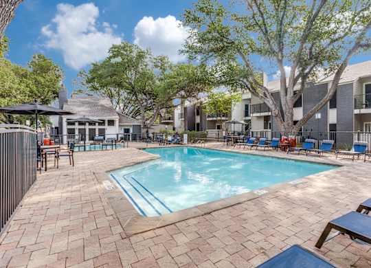 A pool surrounded by a brick patio and lounge chairs.