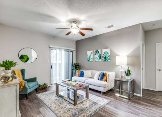 A living room with a white couch, a glass coffee table, and a ceiling fan.