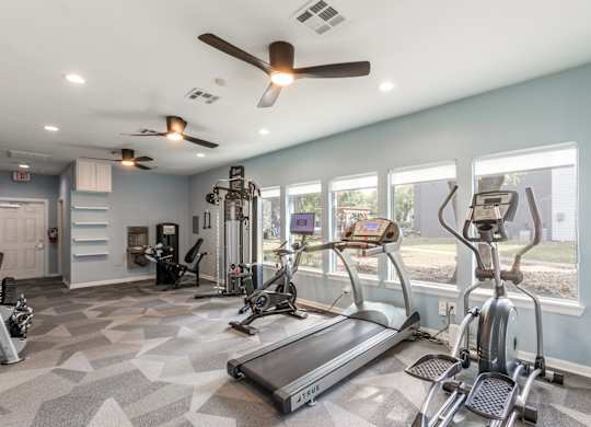 A spacious gym with treadmills, elliptical machines, and a fan.