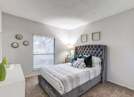 A bedroom with a large bed and a window with blinds.
