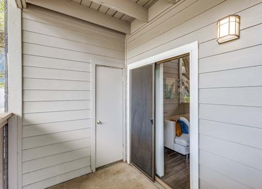 A white door with a glass window is open to a room with a couch and a lamp.