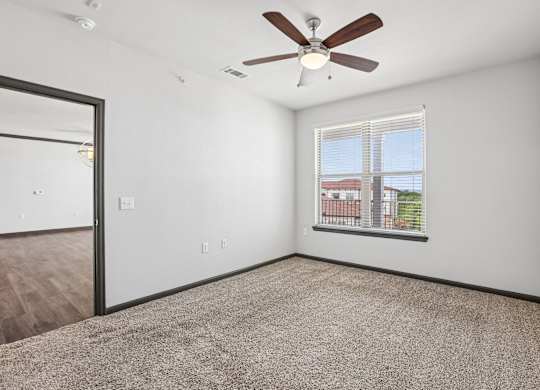 A room with a ceiling fan and a window overlooking a cityscape.