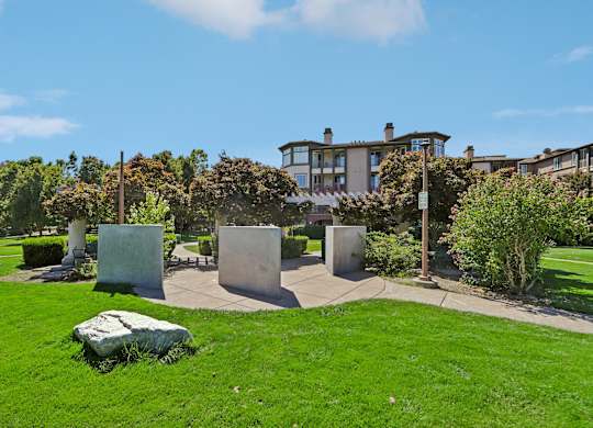 A green lawn with a large rock in the foreground and a building in the background.