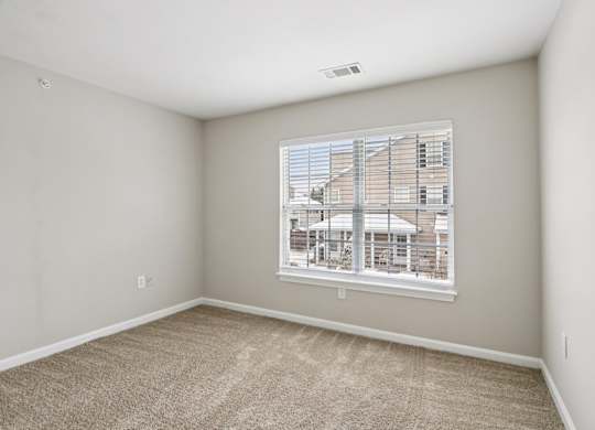 A room with a carpeted floor and a window showing a building outside.