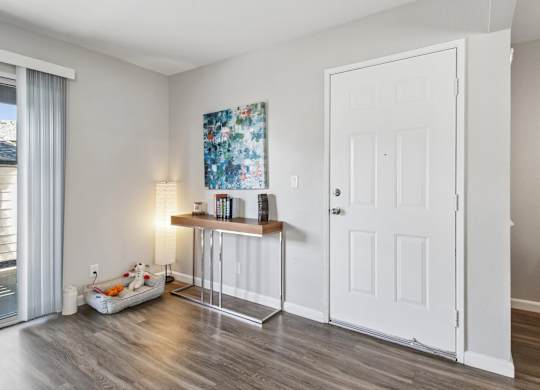 A room with a white door, a table with a lamp and a painting on the wall.