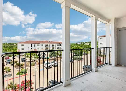 A balcony with a black railing overlooks a parking lot and buildings.