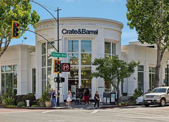 A Crate & Barrel store is shown with people walking by and a car parked in front.