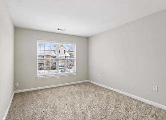 A room with a carpeted floor and a window overlooking a parking lot.