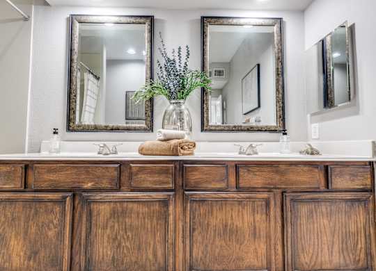 A wooden vanity with a vase of flowers and two mirrors above it.
