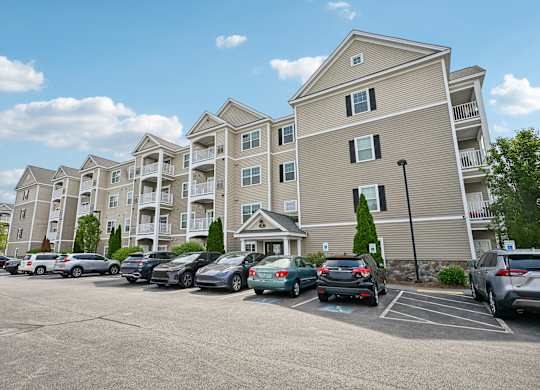 A parking lot in front of a large apartment building with cars parked.