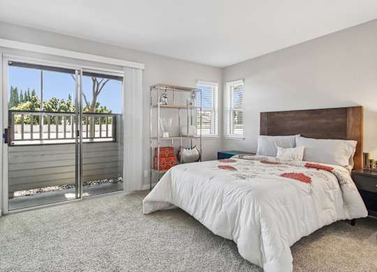 A bedroom with a large bed and a sliding glass door leading to a balcony.
