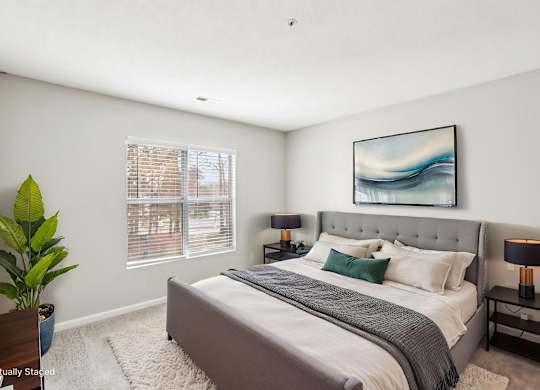 A bedroom with a large bed, a potted plant, and a painting on the wall.