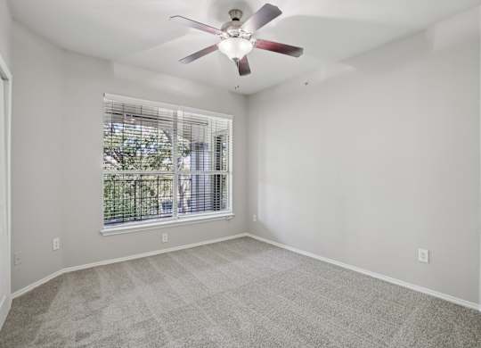 A room with a ceiling fan and a window with blinds.