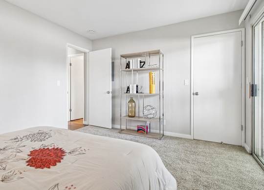 A white bedroom with a bed and a shelf with letters and bottles.