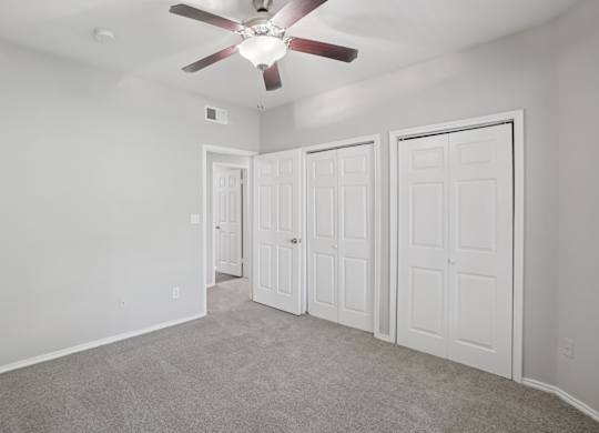 A room with a ceiling fan and three doors.