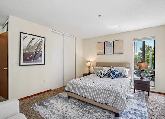 A bedroom with a bed, nightstand, and a painting on the wall.