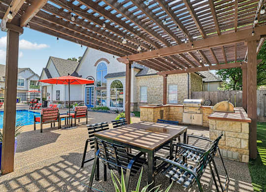A wooden table and chairs are set up under a pergola in a backyard.