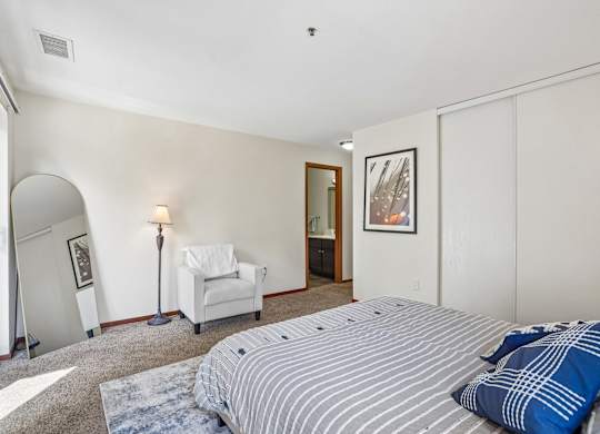 A bedroom with a bed, chair, and painting.