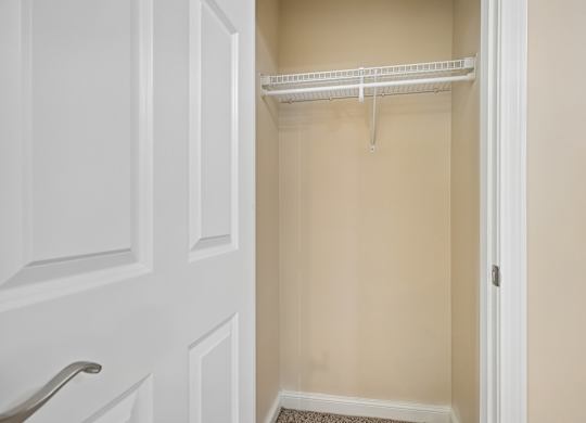 A white closet with a shelf and a white door.