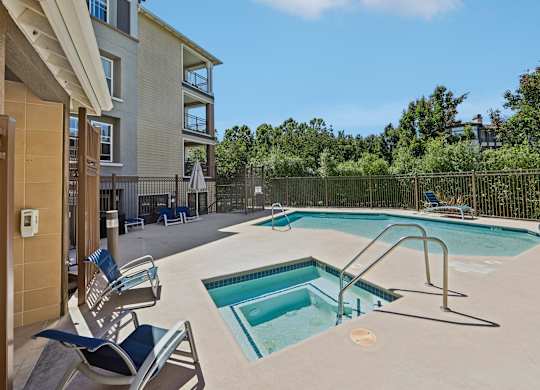 A swimming pool surrounded by a fence and chairs in front of a building.