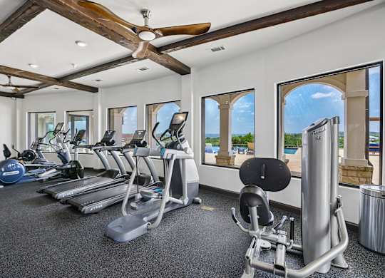 A gym with a row of treadmills and a fan.