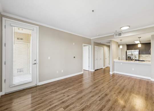 A room with wooden floors and a kitchen area in the background.