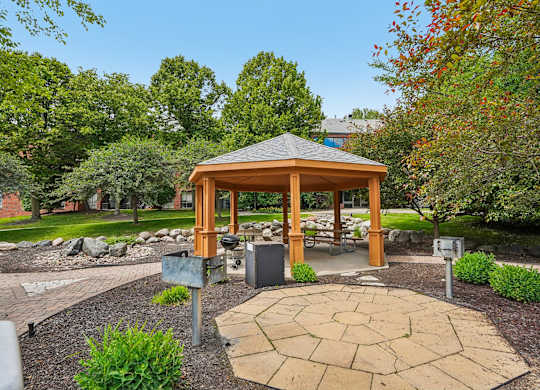 A gazebo is surrounded by a circular brick patio and a variety of plants.