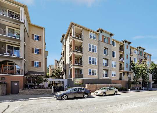 A street view of a residential area with cars parked on the side of the road and apartment buildings in the background.