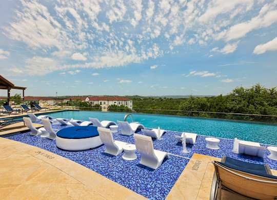 A pool with blue tiles and white chairs.