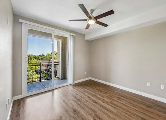 A room with a ceiling fan and sliding glass doors leading to a balcony.